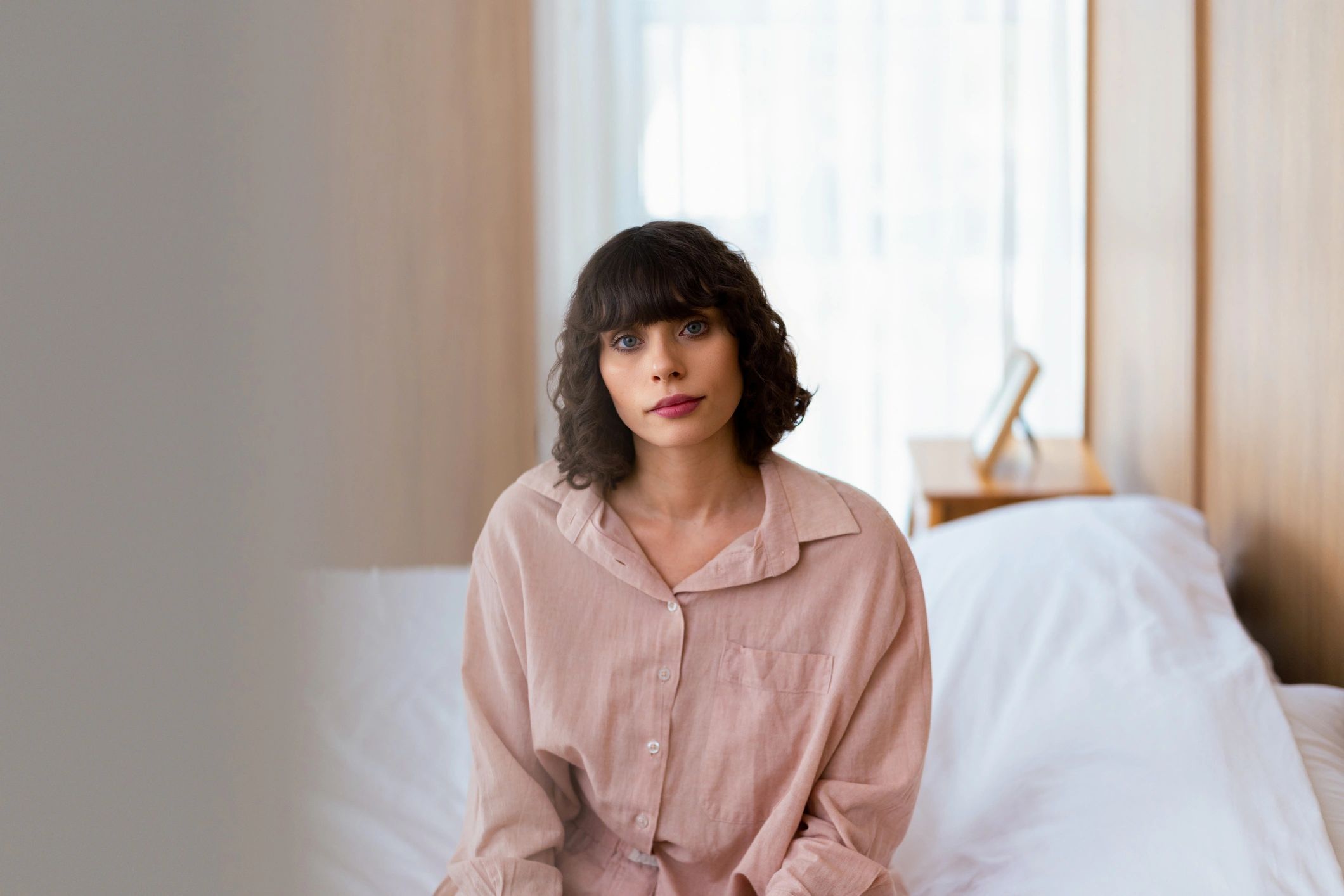 Thoughtful woman sitting on a bed in soft morning light